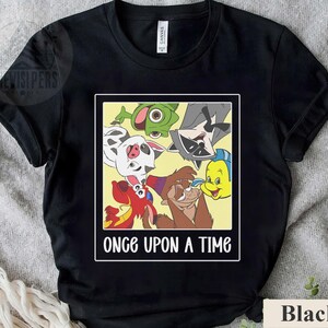 Op de afbeelding: Zwart T-shirt met een rechthoekige afbeelding met tekenfilmfiguren en de tekst "ONCE UPON A TIME" in het wit. De afbeelding bevat een Dalmatische hond, een wasbeer en andere geanimeerde figuren.