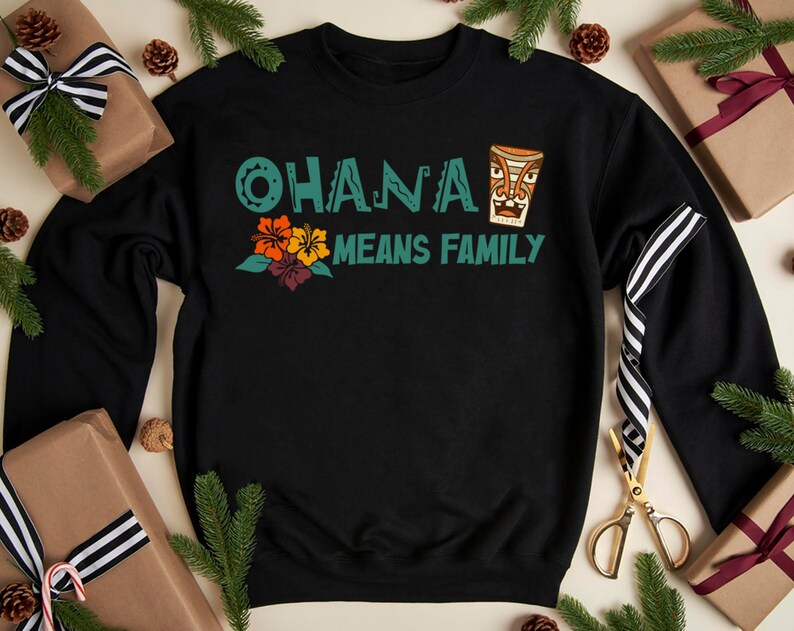 May include: Black sweatshirt with the text "OHANA MEANS FAMILY" in teal and a tiki design. The design includes orange, yellow, and purple flowers. The sweatshirt is surrounded by wrapped gifts and pine branches.