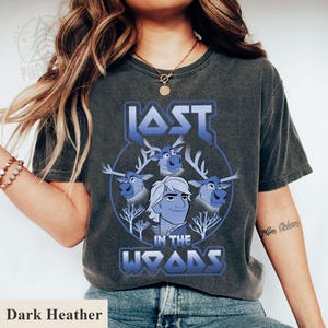May include: Dark heather grey t-shirt with a graphic print of a cartoon character with reindeer. The text "LOST IN THE WOODS" is printed in blue and white.