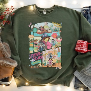 May include: Olive green sweatshirt with a colorful graphic featuring cartoon animals and the text "Undercover Mission." The graphic includes the phrase "Track down the snake!" A red mug with a white holiday design is visible.