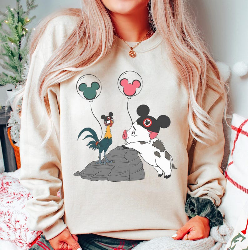 May include: Beige crew neck sweatshirt with a cartoon illustration of a rooster, a pig, and two balloons with Mickey Mouse ears. The pig is wearing a black hat with a red Mickey Mouse emblem. The rooster is standing on a grey rock.