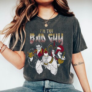 May include: A dark grey t-shirt with a distressed graphic print of Disney villains. The text "I'm the Bad Guy" is printed in gold and red letters. The villains featured are Scar, Ursula, Jafar, and Captain Hook.