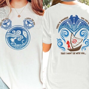 May include: White t-shirt with a blue graphic design on the front and back. The front design features a Mickey Mouse-shaped design with text that says "COME THAT MAY" and "I KNOW THE WAY". The back design includes a boat and the text "THERE IS NOWHERE YOU CAN GO THAT I WON'T BE WITH YOU..."