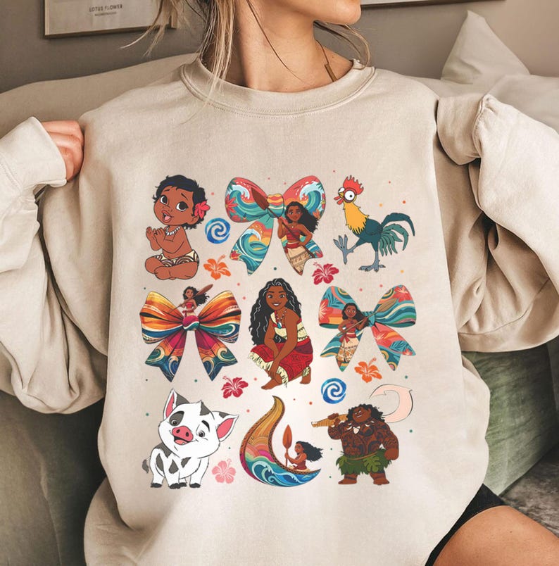 May include: Beige sweatshirt featuring colorful illustrations of characters and elements from a popular animated film. The design includes images of a baby, a rooster, a pig, and a woman, along with decorative bows and floral accents.