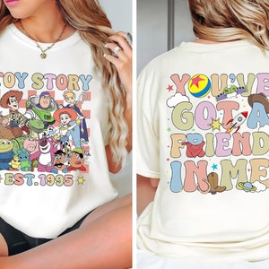 Puede incluir: Camiseta blanca con un gr&aacute;fico colorido de los personajes de Toy Story en la parte delantera y el texto "Toy Story Est. 1995". La parte posterior de la camiseta tiene un gr&aacute;fico colorido con el texto "You've Got A Friend In Me".