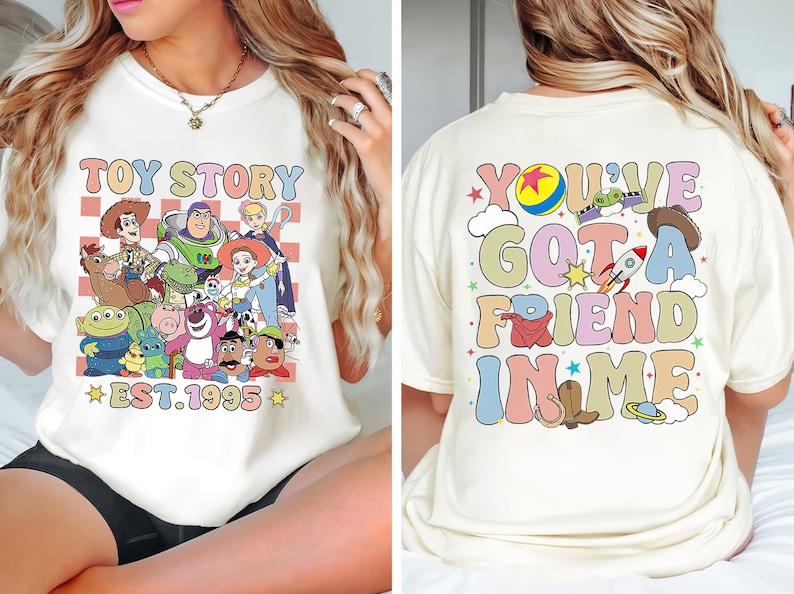 Puede incluir: Camiseta blanca con un gr&aacute;fico colorido de los personajes de Toy Story en la parte delantera y el texto "Toy Story Est. 1995". La parte posterior de la camiseta tiene un gr&aacute;fico colorido con el texto "You've Got A Friend In Me".