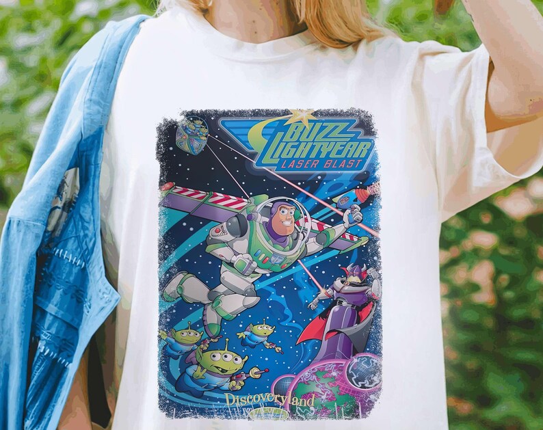 Puede incluir: Camiseta blanca con un gr&aacute;fico de estilo vintage de Buzz Lightyear de la franquicia Toy Story. El gr&aacute;fico presenta a Buzz en su traje de ranger espacial, volando por el espacio con un disparo l&aacute;ser. El texto "Buzz Lightyear Laser Blast" est&aacute; impreso sobre el gr&aacute;fico, y "Discoveryland" est&aacute; impreso debajo.