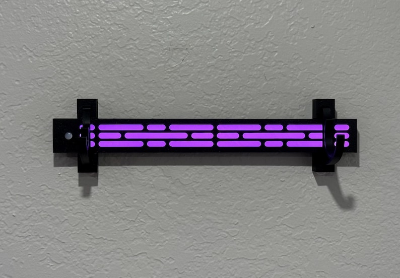 Puede incluir: Una l&aacute;mpara de pared negra con una serie de luces p&uacute;rpuras horizontales. La l&aacute;mpara es rectangular con una serie de recortes. La l&aacute;mpara est&aacute; montada en una pared gris texturizada.