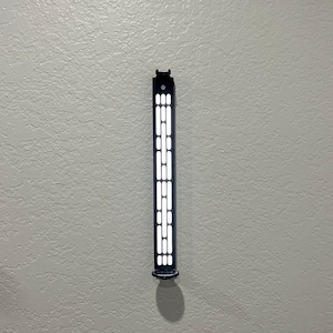 May include: A black wall-mounted light fixture with a rectangular design. The fixture has a series of rectangular and circular cutouts that emit light. The fixture is mounted on a textured, light gray wall.