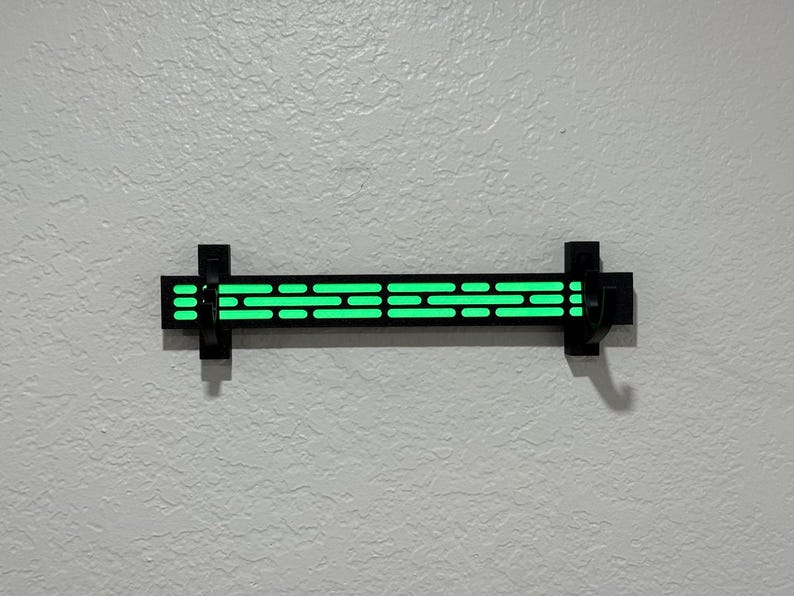 Puede incluir: Una l&aacute;mpara de pared negra con un brillo verde ne&oacute;n. La l&aacute;mpara tiene una serie de recortes rectangulares horizontales que emiten luz. La l&aacute;mpara est&aacute; montada en una pared texturizada de color blanco roto.