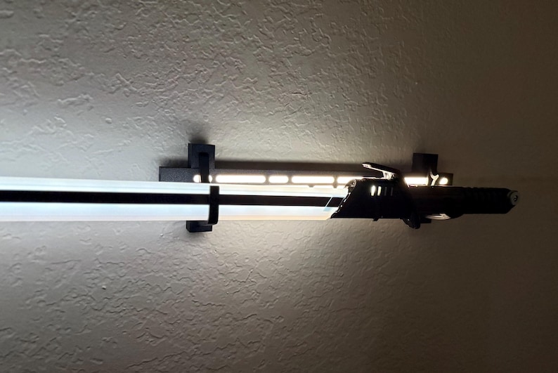 Puede incluir: Una moderna l&aacute;mpara LED en blanco y negro montada en una pared texturizada. La l&aacute;mpara tiene forma rectangular con una tira de luz blanca brillante y un acento negro. Se sujeta con soportes negros.