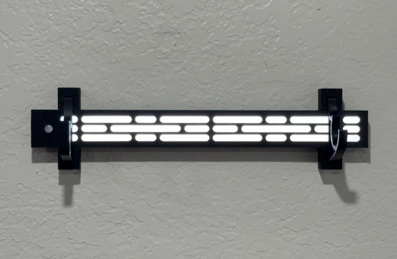 Puede incluir: Decoraci&oacute;n de pared negra con una serie de luces blancas rectangulares horizontales. Las luces est&aacute;n dispuestas en un patr&oacute;n a trav&eacute;s de una barra rectangular negra. La decoraci&oacute;n est&aacute; montada en una pared gris claro con soportes negros.