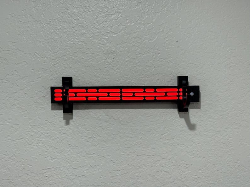 Puede incluir: Una l&aacute;mpara de pared negra con una serie de luces rojas rectangulares horizontales. La l&aacute;mpara est&aacute; montada en una pared gris claro texturizada. La l&aacute;mpara mide aproximadamente 30 cm de largo.