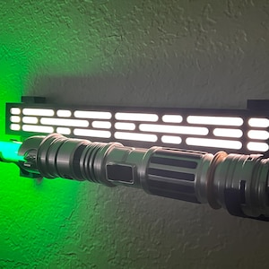 May include: A black lightsaber wall mount with a green lightsaber attached. The mount has a white light grid pattern.