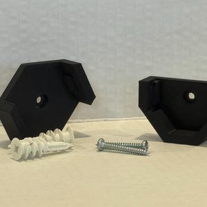 May include: Two black, angled shelf brackets with mounting holes. Includes white wall anchors and a silver screw for installation. The brackets are designed to support a shelf.