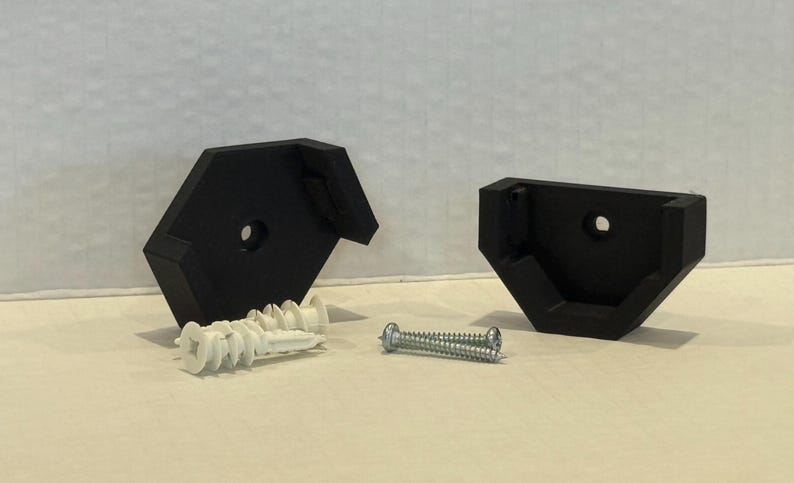May include: Two black, angled shelf brackets with mounting holes. Includes white wall anchors and a silver screw for installation. The brackets are designed to support a shelf.
