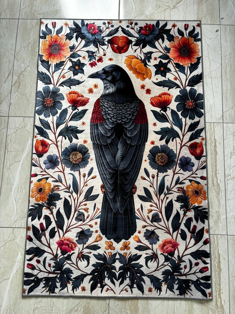 May include: A black raven with a red breast is depicted in the centre of a white rug with a floral pattern. The flowers are in shades of red, orange, yellow, and blue.