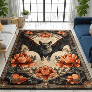 May include: A black and white rug with a floral design and a bat in the centre. The bat is black with orange eyes and is surrounded by orange flowers. The rug has a black border with a gold trim.