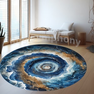 Op de afbeelding: Een rond abstract blauw en gouden tapijt met een draaiend patroon. Het tapijt heeft een wit midden met een gouden cirkel in het midden.