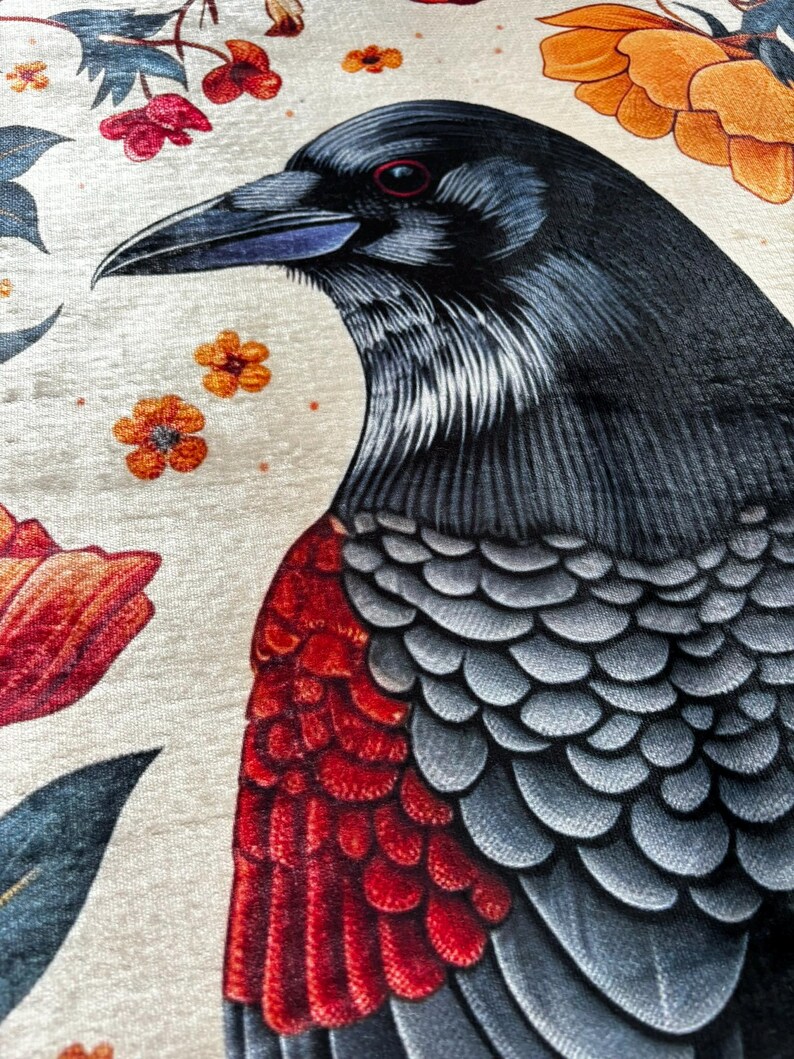 May include: Detailed fabric design featuring a raven illustration. The raven has black and grey feathers, a red chest, and a sharp beak. The background is cream-coloured with orange and red floral accents.