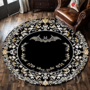 Puede incluir: Alfombra redonda negra y dorada con una silueta de murciélago blanco en el centro. La alfombra tiene un patrón floral con detalles intrincados.
