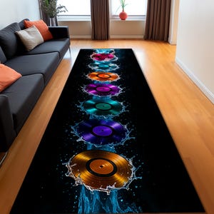 May include: A rectangular black rug featuring a series of colorful vinyl records with water splashes. The records are in shades of red, orange, purple, green, and gold. The rug is placed on a hardwood floor.