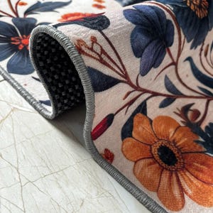 May include: Close-up of the edge of a rug with a floral pattern. The rug has a gray border and a white background with orange, red, and blue flowers.