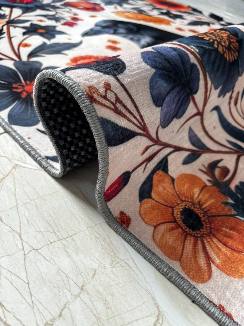 May include: Close-up of the edge of a rug with a floral pattern. The rug has a gray border and a white background with orange, red, and blue flowers.