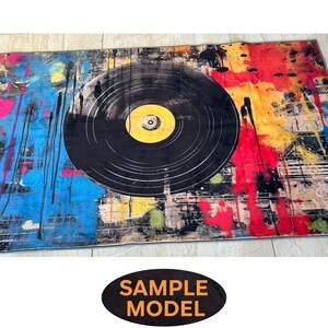 K&ouml;nnte beinhalten: Ein bunter Teppich mit einem gro&szlig;en schwarzen Schallplatten-Design. Der Teppich hat Spritzer in Gelb, Rot, Blau und Gr&uuml;n.