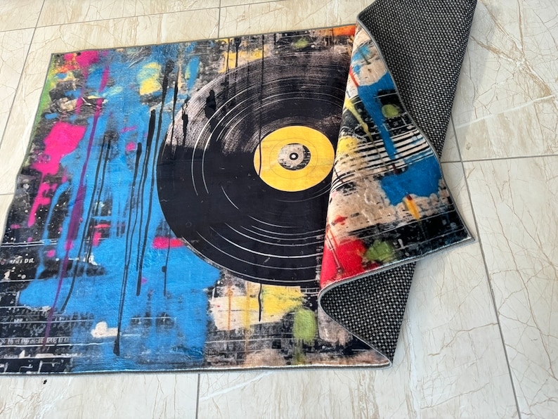 K&ouml;nnte beinhalten: Ein bunter Teppich mit einem gro&szlig;en schwarzen Schallplatten-Design. Der Teppich hat ein schwarz-wei&szlig; gestreiftes Muster an der Seite und eine schwarze R&uuml;ckseite.