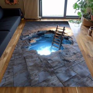 Op de afbeelding: Een rechthoekig vloerkleed met een 3D-illusieontwerp. Het kleed toont een gat in een houten vloer, dat een gloeiend blauw licht en een houten ladder onthult. Het kleed heeft grijze, blauwe en bruine tinten.