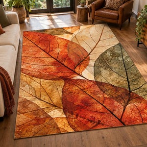 May include: A rectangular area rug featuring a large-scale print of overlapping autumn leaves in shades of burnt orange, deep red, golden yellow, and muted olive green, with visible dark vein patterns across the surface of each leaf.