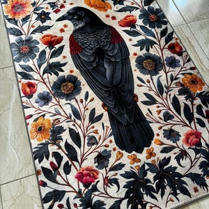 May include: A black raven with a red breast sits in the center of a floral design rug. The rug has a white background with black, red, yellow, and blue flowers.
