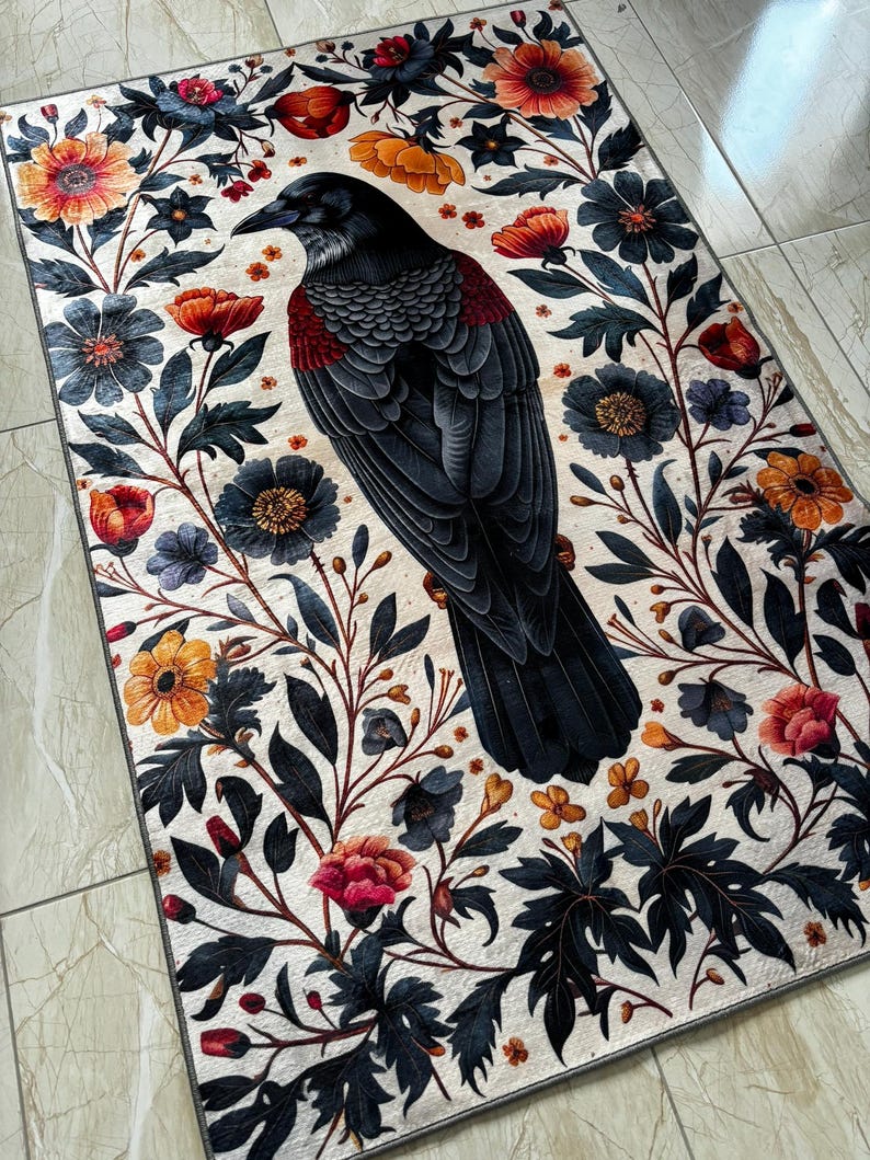 May include: A black raven with a red breast sits in the center of a floral design rug. The rug has a white background with black, red, yellow, and blue flowers.