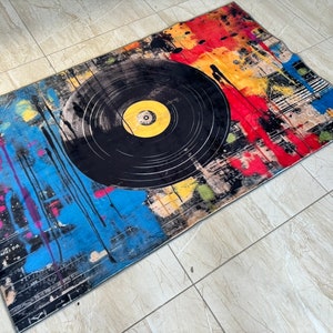 K&ouml;nnte beinhalten: Ein bunter Teppich mit einem schwarzen Schallplatten-Design. Der Teppich hat Spritzer in Rot, Gelb, Blau und Pink.