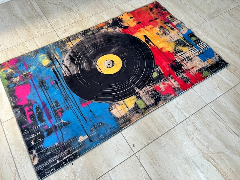 K&ouml;nnte beinhalten: Ein bunter Teppich mit einem schwarzen Schallplatten-Design. Der Teppich hat Spritzer in Rot, Gelb, Blau und Pink.