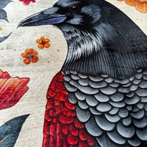 May include: A black crow with red and gray feathers, perched on a white background with orange and red flowers.