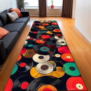 May include: A rectangular area rug featuring a pattern of colorful vinyl records on a black background. The records are in various colors, including red, orange, yellow, green, and white. The rug is placed on a wooden floor.