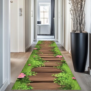 Op de afbeelding: Een gang met een houten vloer en een deur aan het einde. Een decoratief tapijt met een pad van houten planken, groen gras en roze bloemen ligt op de vloer.