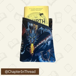 May include: A black quilted book sleeve with a dragon design. The sleeve has a zipper closure and is holding a yellow paperback book with the title "Graduate or Die" and the author "Jennifer L. Armentrout".