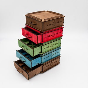 Può includere: Una pila di scatole di legno colorate, marrone, rosso, verde e blu. Ogni scatola ha un cassetto e un coperchio, con decorazioni a forma di stella. I cassetti sono aperti, rivelando i compartimenti interni.