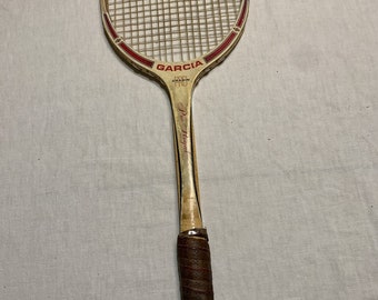 以下が含まれることがあります： 木製のフレームと茶色の革製グリップを備えた、ヴィンテージのGarcia Pro Royalテニスラケット。ラケットには赤と白のアクセントがあり、「GARCIA」のブランド名が見えます。