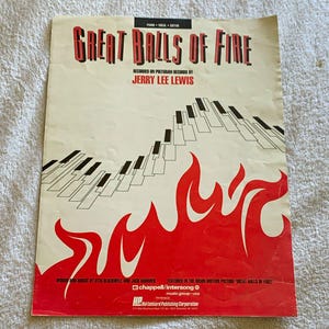 May include: A vintage sheet music cover for Great Balls of Fire by Jerry Lee Lewis. The cream-colored paper features red flame graphics at the bottom, a black and white piano keyboard illustration, and black text detailing the song and artist.