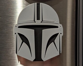May include: A gray and black 3D printed Mandalorian helmet. The helmet is a popular character from the Star Wars franchise.