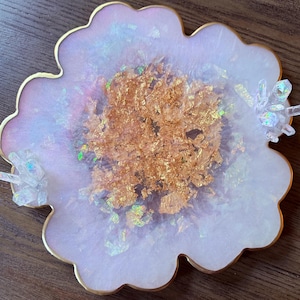 May include: A white and pink resin tray with a gold leaf design and clear crystal accents. The tray has a scalloped edge and a gold rim.