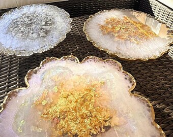 May include: Three round resin serving trays with gold leaf accents. The trays are white with a slightly iridescent finish. The trays are on a woven wicker surface.