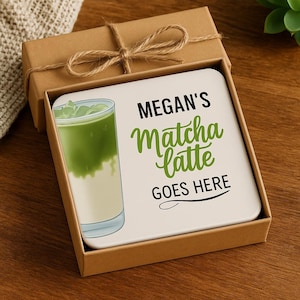 May include: A square white coaster with a matcha latte illustration and the text "MEGAN'S Matcha latte GOES HERE" is presented in a brown gift box tied with twine. The matcha latte is green and white.