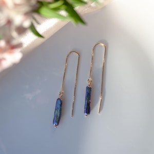 May include: A pair of gold chain earrings with a dark blue baroque pearl pendant on each chain.