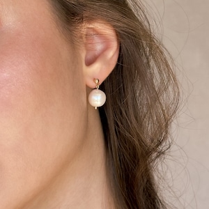 May include: A pair of gold stud earrings with a single white pearl dangling from each earring.