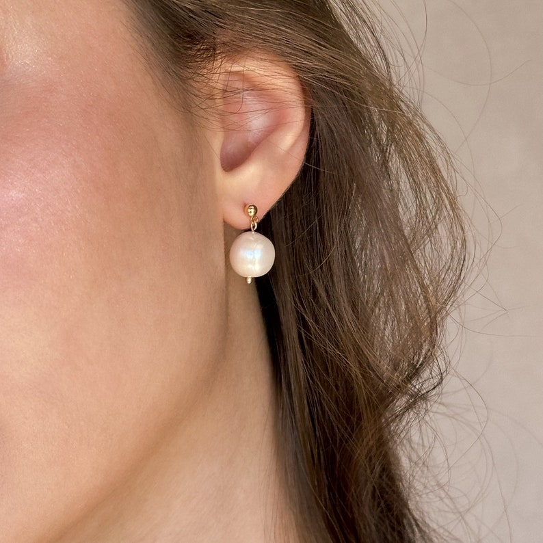 May include: A pair of gold stud earrings with a single white pearl dangling from each earring.
